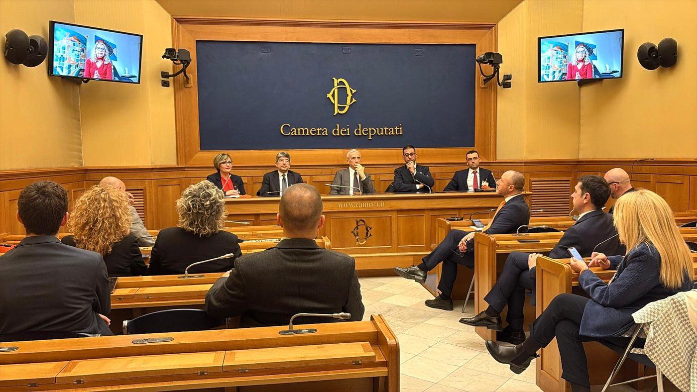 La Sala Stampa della Camera dei Deputati durante la conferenza, con il pubblico e un collegamento video